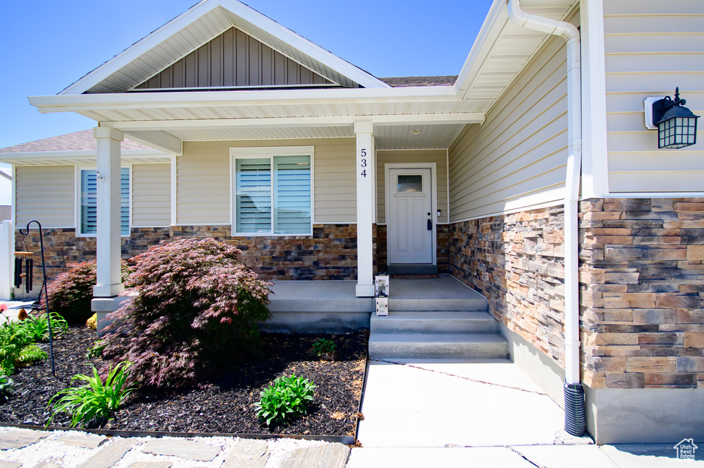 Entrance to property featuring stone siding, covered porch, and roof with shingles