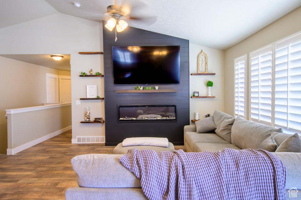 Living room with vaulted ceiling, wood finished floors, a ceiling fan, a glass covered fireplace, and baseboards