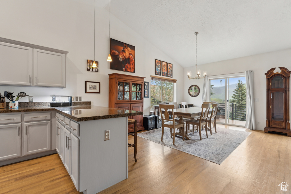 Kitchen with high vaulted ceiling, a peninsula, a chandelier, and light wood finished floors
