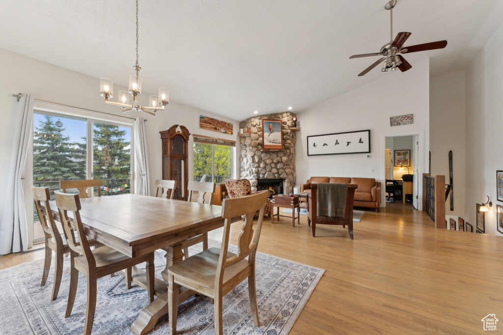 Dining room with lofted ceiling, healthy amount of natural light, light wood-style floors, a fireplace, and a chandelier