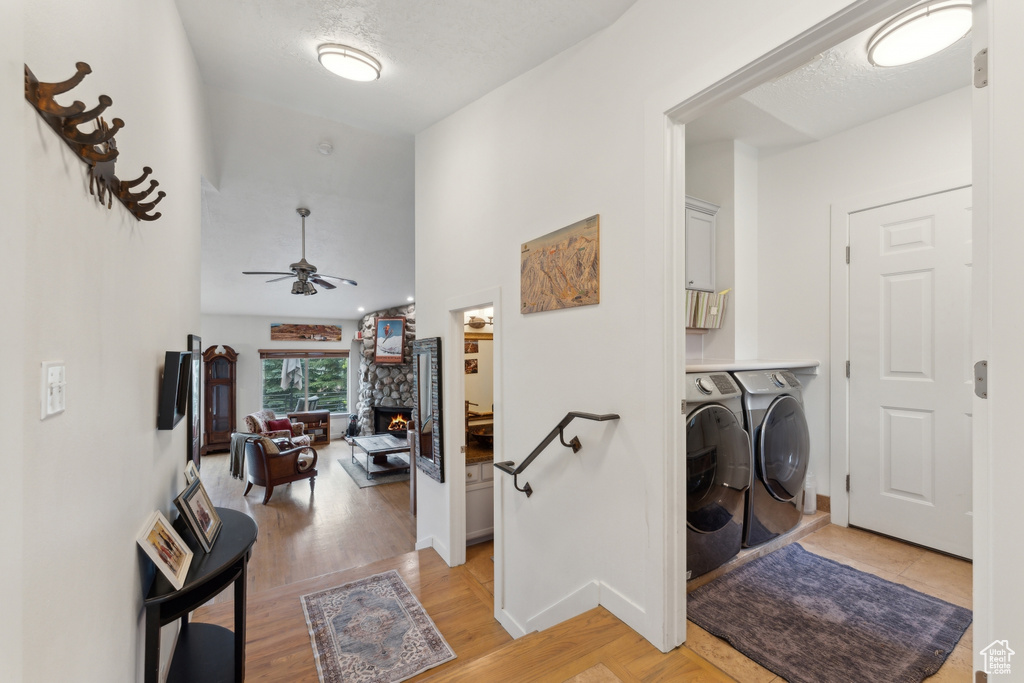 Laundry area with washer and clothes dryer, cabinet space, a stone fireplace, a ceiling fan, and light wood-style floors