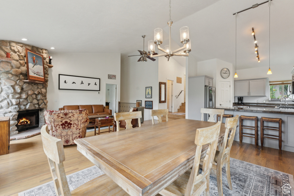 Dining area with light wood-style floors, a chandelier, a stone fireplace, and a towering ceiling
