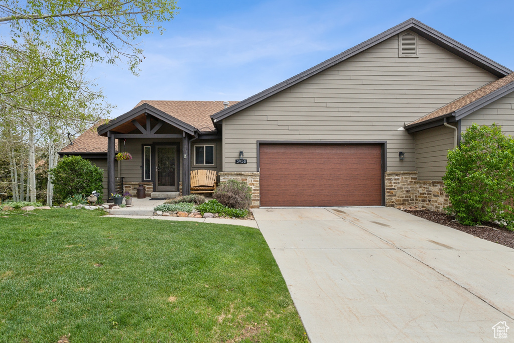 View of front of home with a garage, a front yard, concrete driveway, roof with shingles, and stone siding