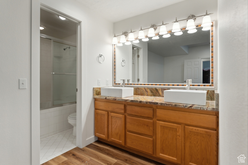 Full bath featuring double vanity, toilet, wood finished floors, and shower / bath combination with glass door