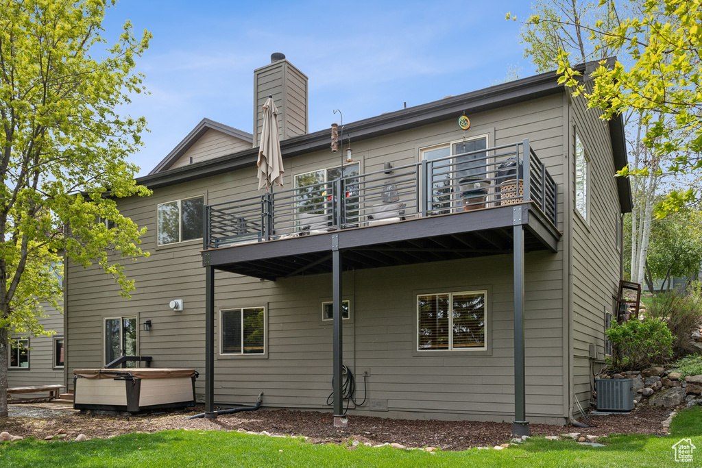 Back of property featuring a balcony, a hot tub, a chimney, and cooling unit