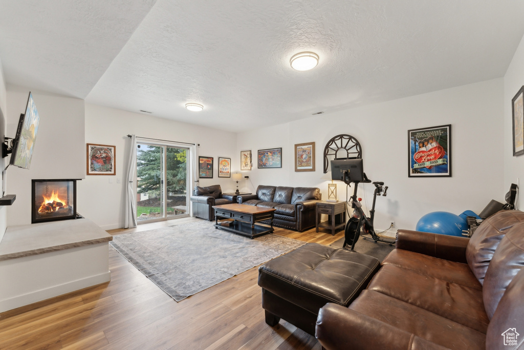 Living room with light wood-style flooring, a textured ceiling, baseboards, and a multi sided fireplace