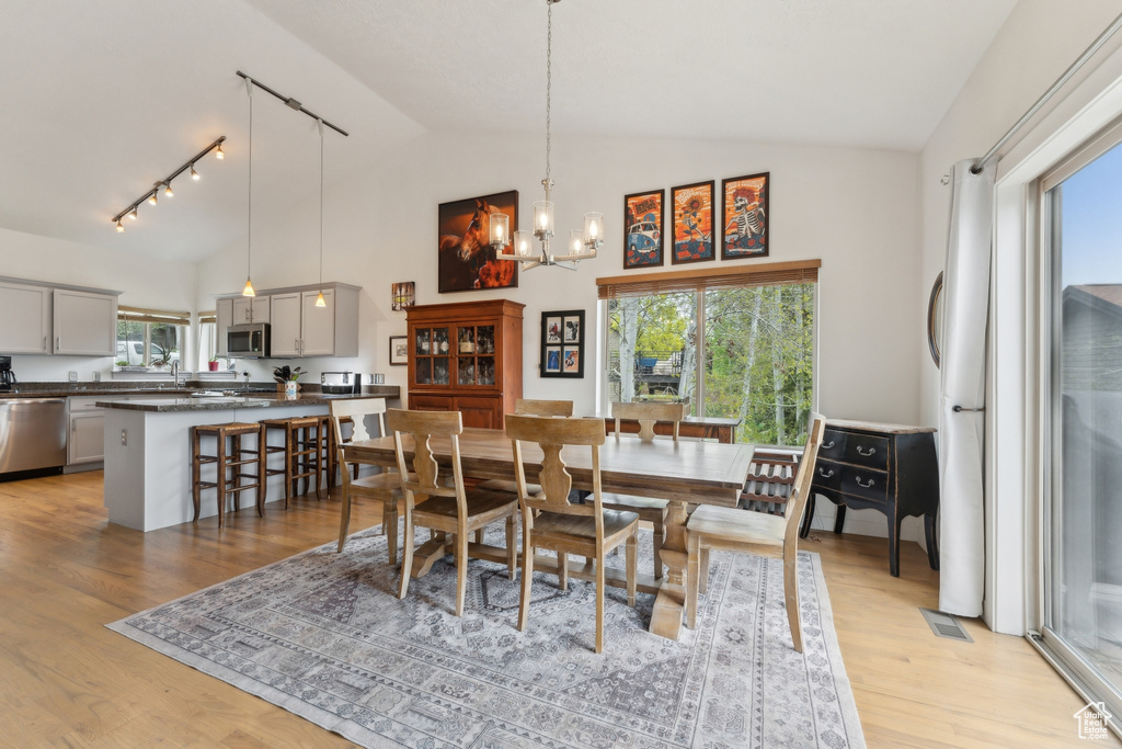 Dining space with rail lighting, light wood-style floors, high vaulted ceiling, and a chandelier
