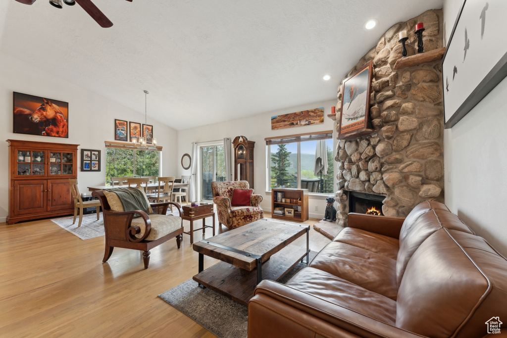 Living room with light wood-type flooring, vaulted ceiling, ceiling fan, a stone fireplace, and recessed lighting