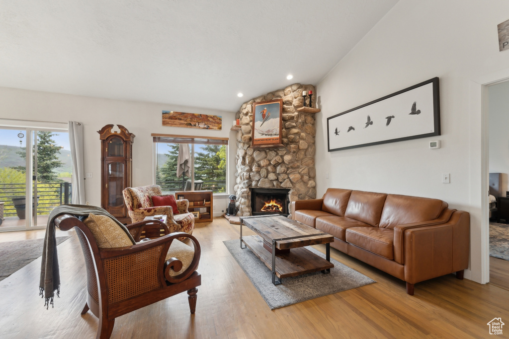 Living room featuring healthy amount of natural light, light wood-style flooring, a stone fireplace, vaulted ceiling, and recessed lighting