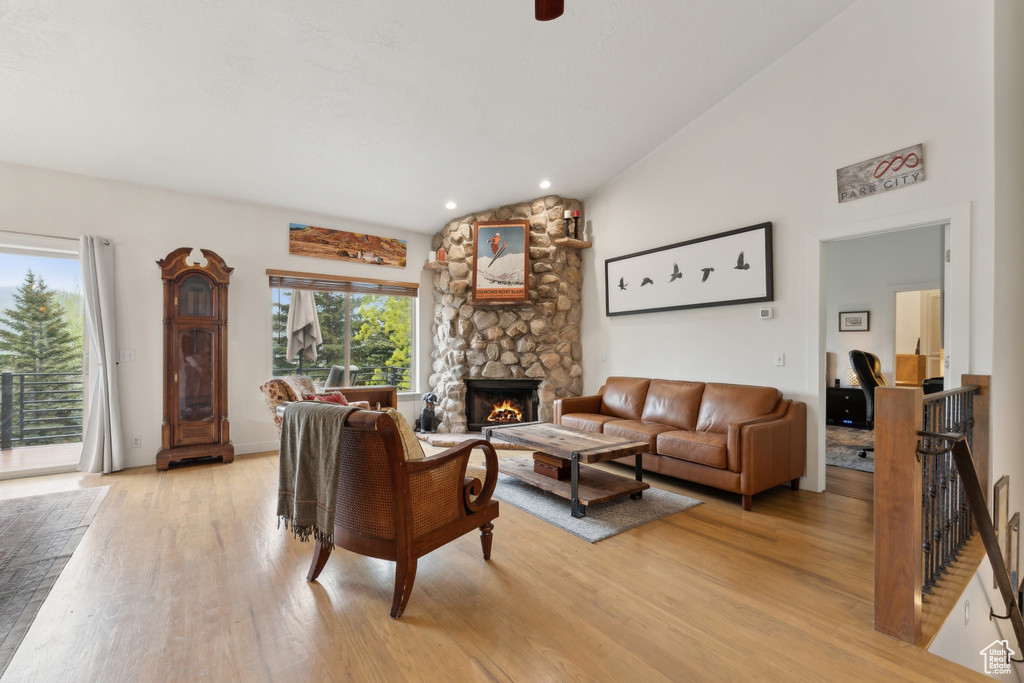 Living room with vaulted ceiling, light wood-style flooring, and a stone fireplace