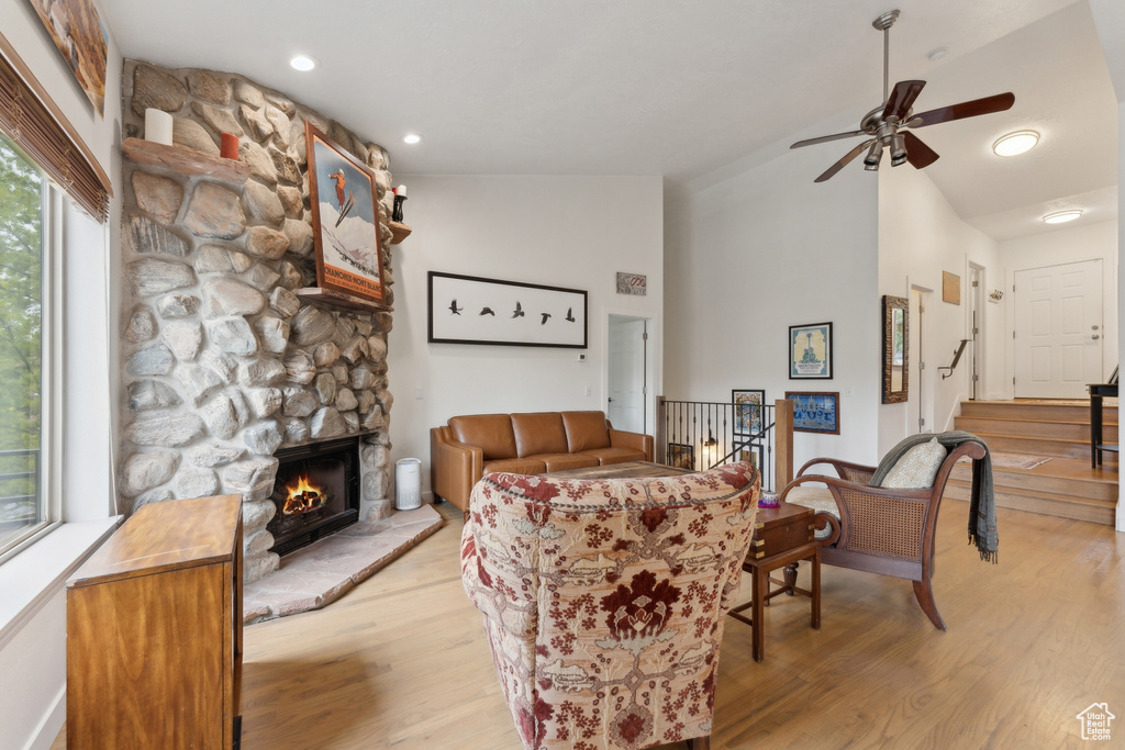 Living area featuring lofted ceiling, light wood-style flooring, a ceiling fan, a fireplace, and stairs