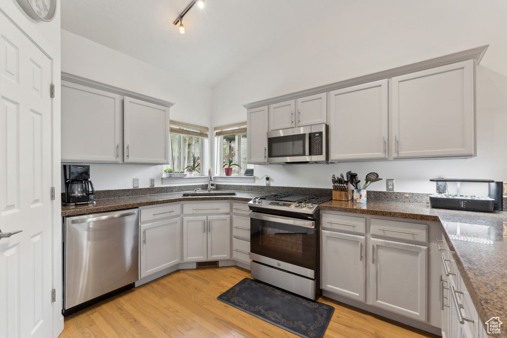 Kitchen featuring appliances with stainless steel finishes, a sink, vaulted ceiling, light wood-style flooring, and gray cabinetry