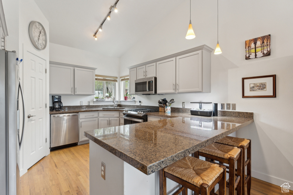 Kitchen featuring stainless steel appliances, a peninsula, light wood-style floors, a breakfast bar area, and hanging light fixtures