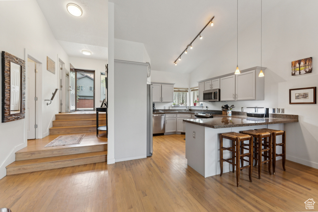 Kitchen featuring appliances with stainless steel finishes, a peninsula, lofted ceiling, a breakfast bar, and light wood-style floors