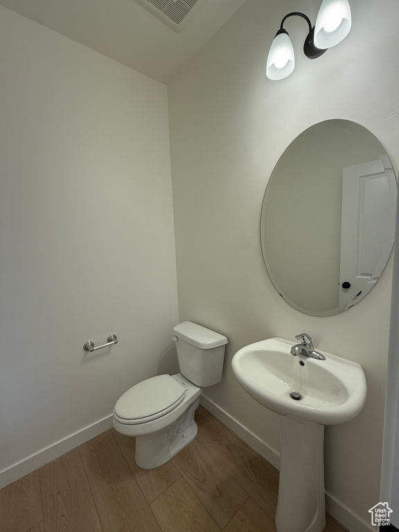 Half bath featuring wood finished floors, toilet, and baseboards