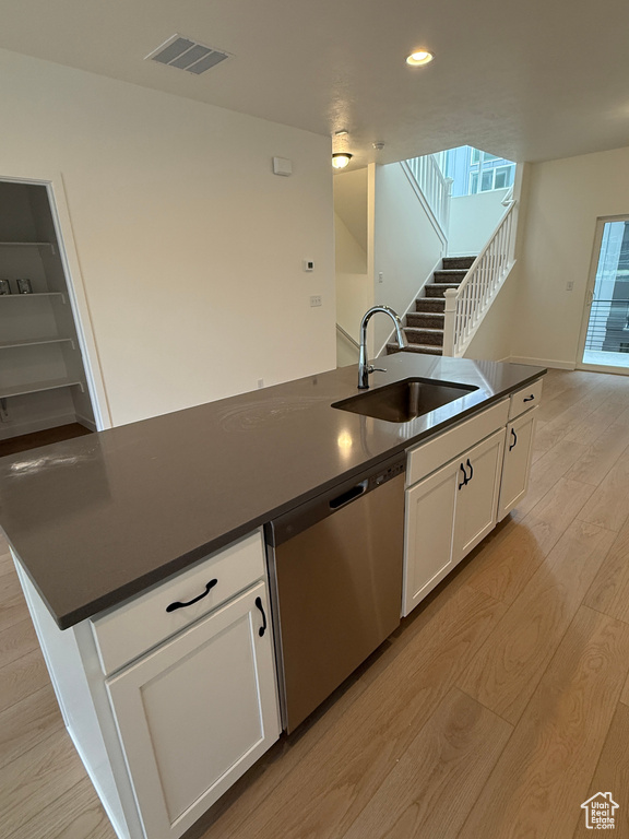 Kitchen with a sink, dishwasher, dark countertops, light wood-type flooring, and white cabinetry