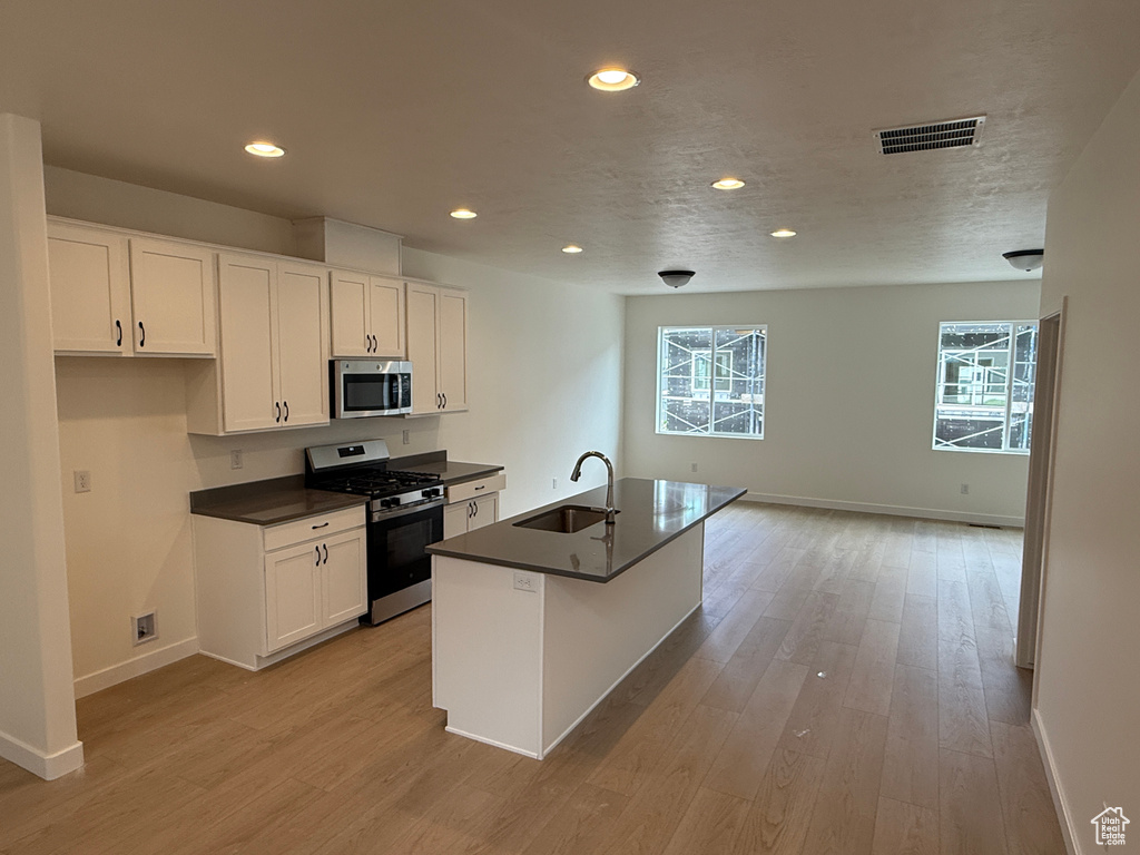 Kitchen featuring stainless steel appliances, a sink, dark countertops, baseboards, and light wood finished floors