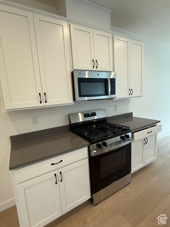 Kitchen featuring stainless steel appliances, light wood finished floors, dark countertops, and white cabinets
