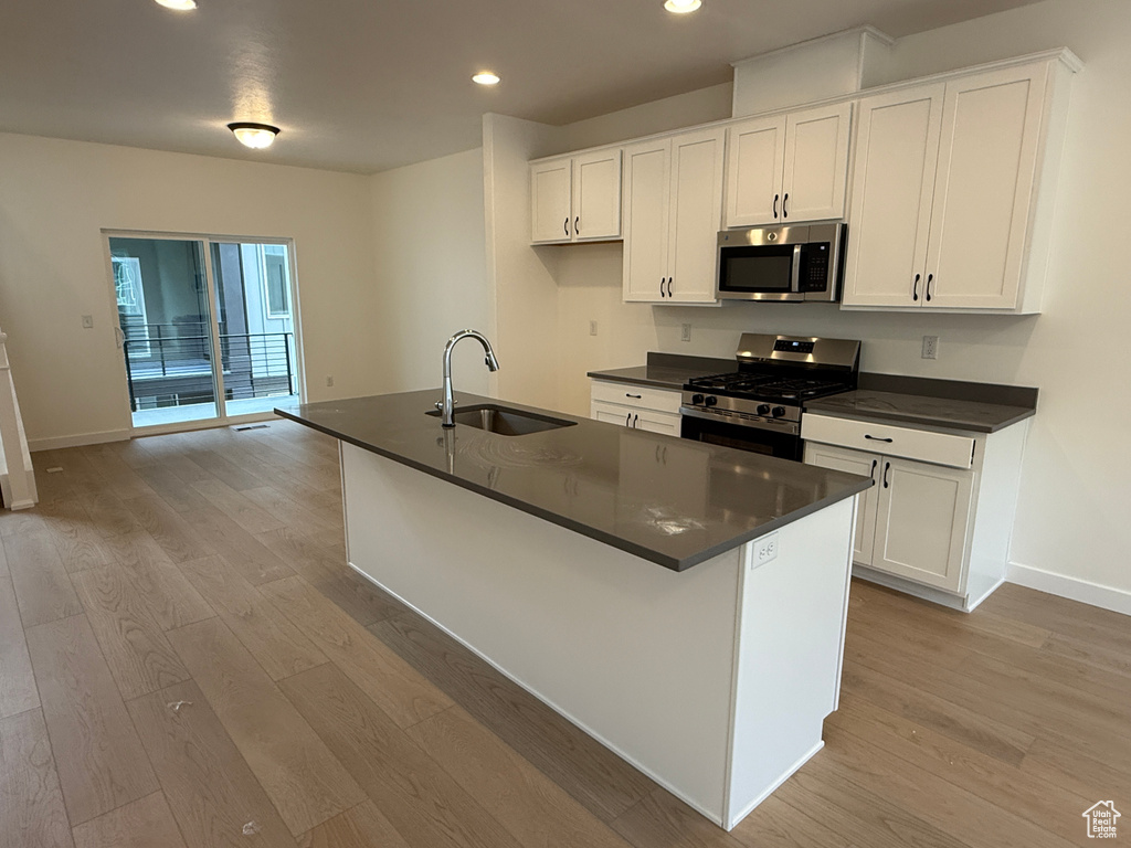 Kitchen featuring a sink, stainless steel appliances, dark countertops, light wood-style floors, and recessed lighting