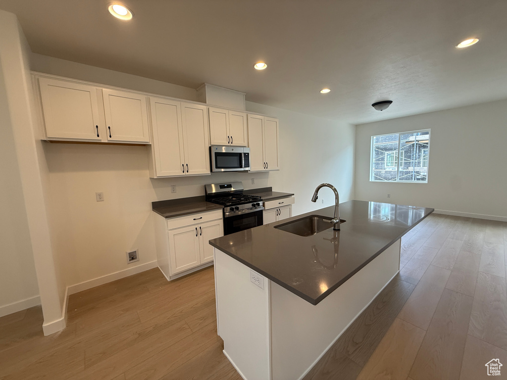 Kitchen featuring appliances with stainless steel finishes, a sink, dark countertops, light wood-type flooring, and white cabinets