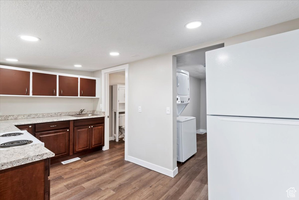 Kitchen with a sink, freestanding refrigerator, stacked washer / drying machine, light wood-type flooring, and light countertops