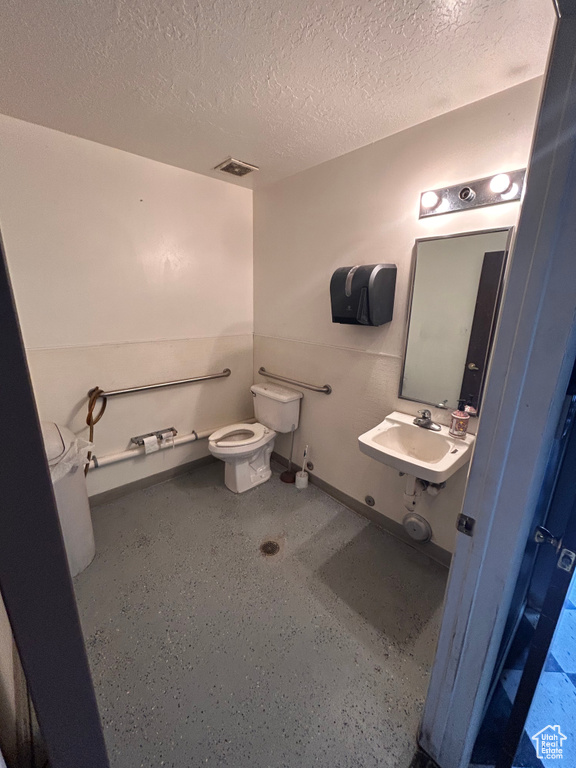 Half bath with toilet, a sink, a textured ceiling, and baseboards