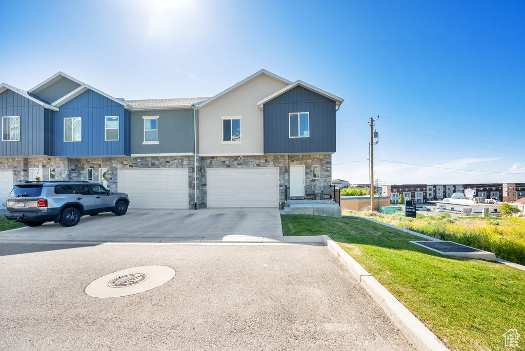 View of property with stone siding, an attached garage, concrete driveway, and a front yard