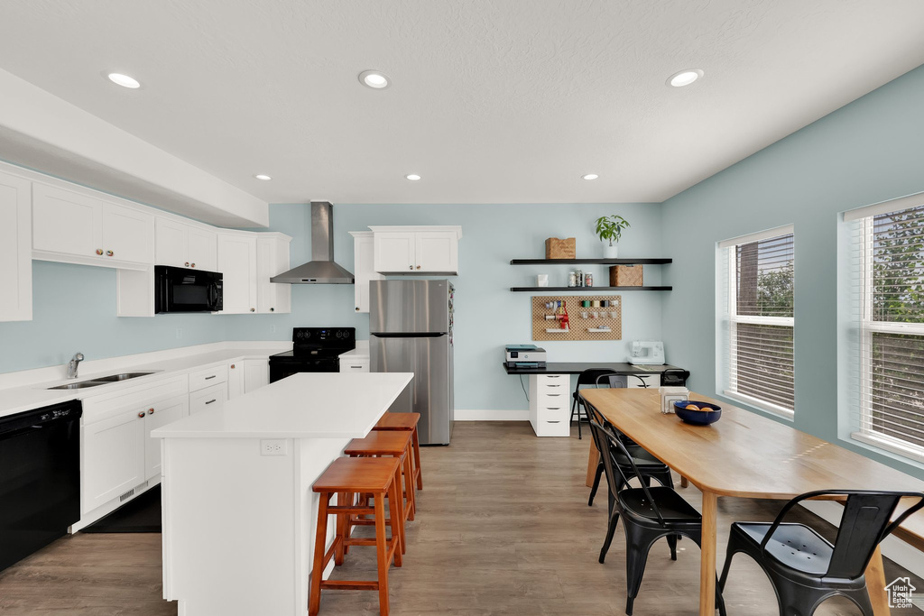 Kitchen featuring wall chimney exhaust hood, black appliances, a sink, white cabinets, and recessed lighting