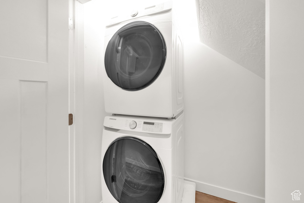 Laundry room with stacked washing machine and dryer and wood finished floors