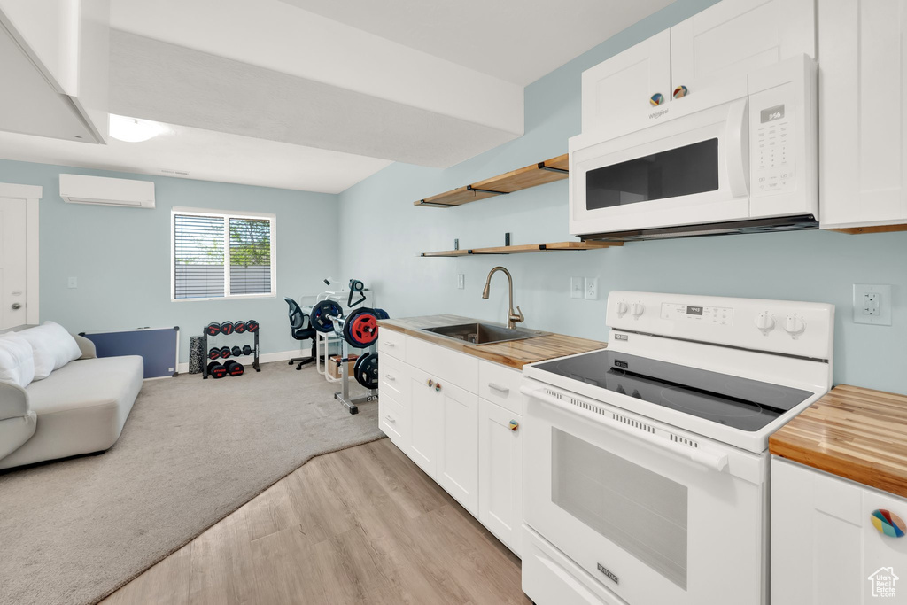 Kitchen featuring white appliances, a sink, butcher block counters, open floor plan, and a wall unit AC