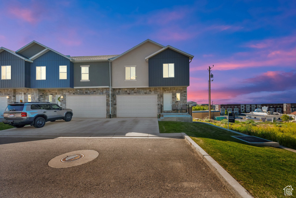 Townhome / multi-family property with stone siding, a garage, driveway, and a lawn