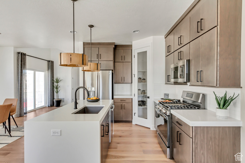 Kitchen featuring stainless steel appliances, a sink, tasteful backsplash, light wood finished floors, and light countertops