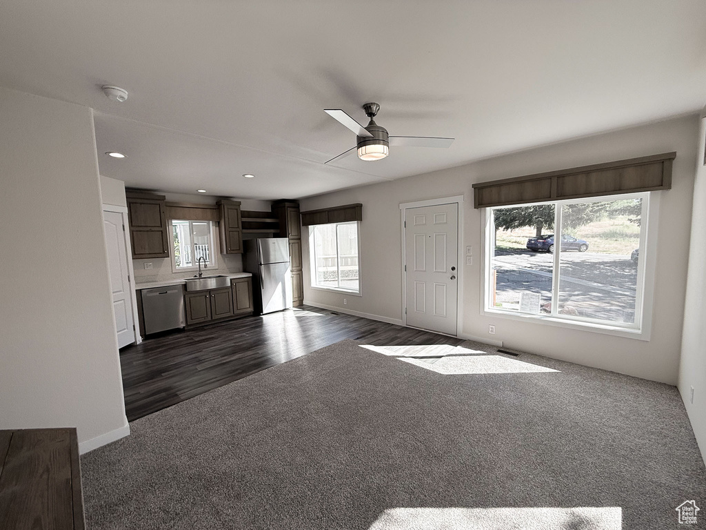 Unfurnished living room featuring a sink, a ceiling fan, dark colored carpet, baseboards, and dark wood-style floors