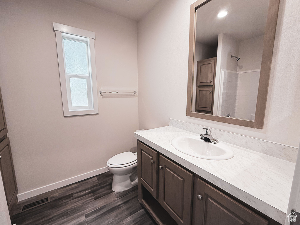 Bathroom featuring vanity, toilet, wood finished floors, a shower, and baseboards