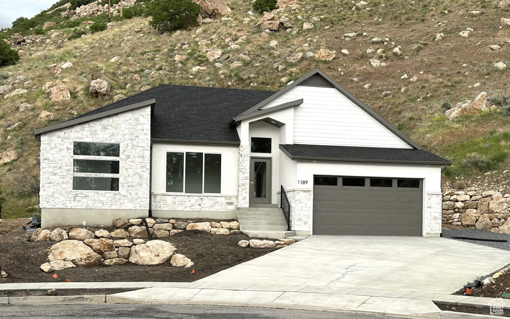 View of front facade featuring stone siding, driveway, a garage, and a shingled roof