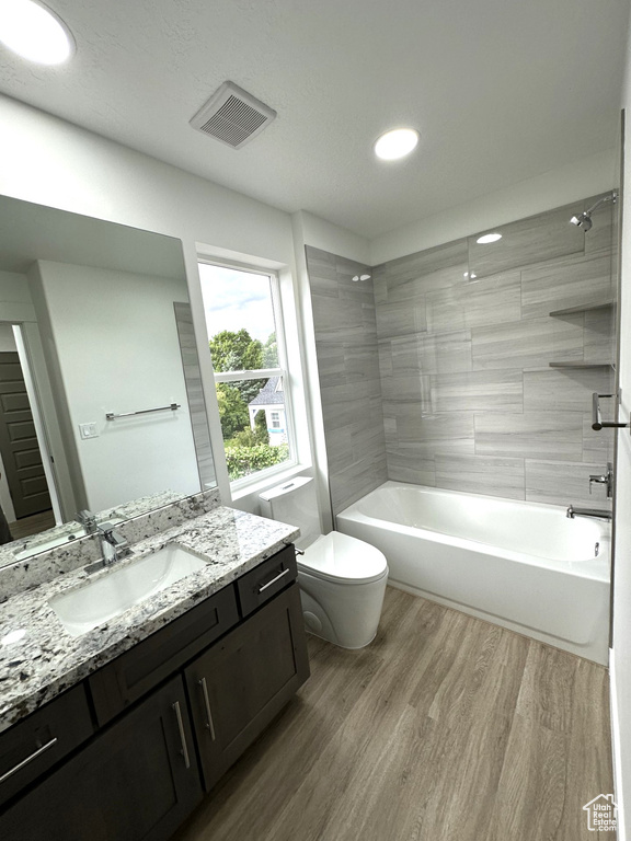 Bathroom featuring toilet, wood finished floors, vanity, tub / shower combination, and recessed lighting