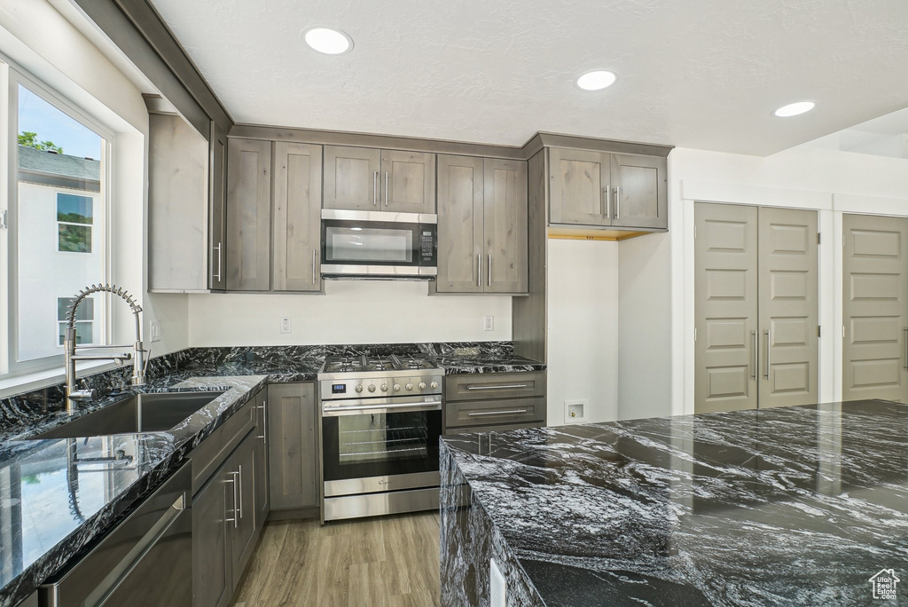 Kitchen with appliances with stainless steel finishes, a sink, dark stone counters, light wood-style flooring, and recessed lighting