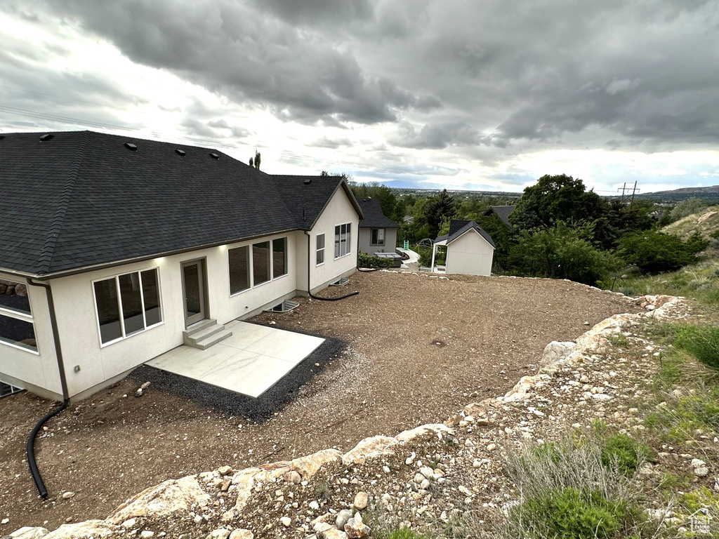 Back of house with a shingled roof, stucco siding, and a patio area