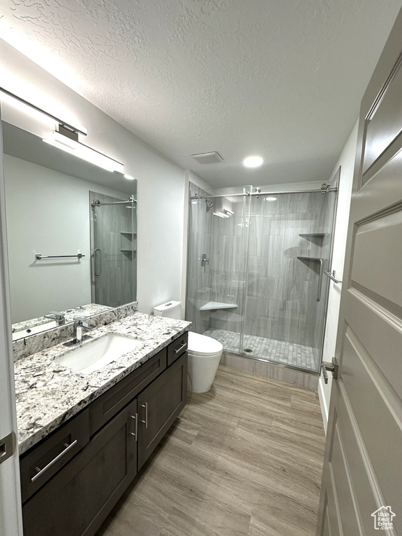 Bathroom with vanity, a stall shower, a textured ceiling, toilet, and wood finished floors