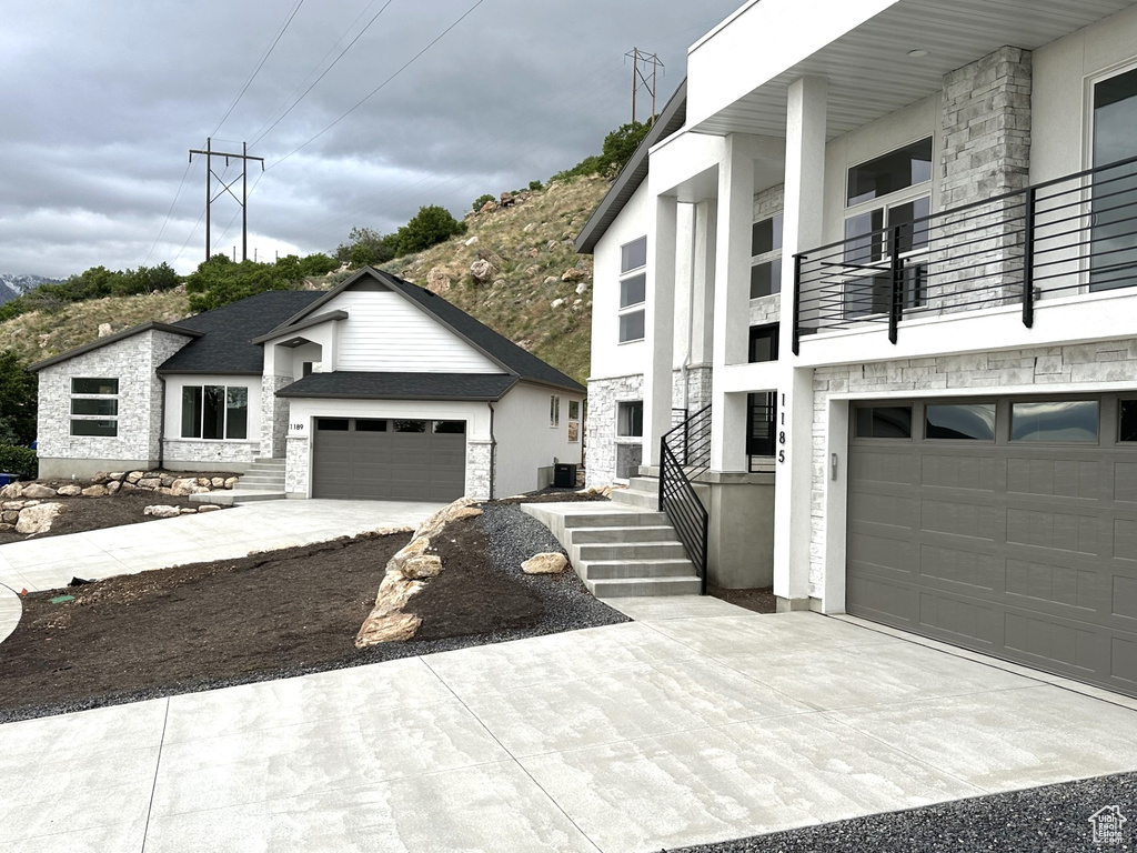 View of front of property with a garage, stone siding, a balcony, and driveway