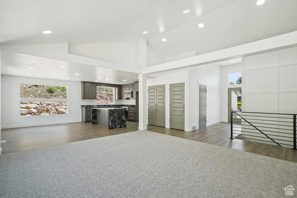 Unfurnished living room featuring recessed lighting, healthy amount of natural light, dark wood-style flooring, a sink, and high vaulted ceiling