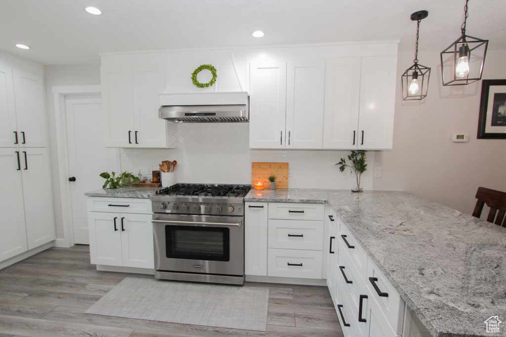 Kitchen featuring high end range, exhaust hood, a peninsula, recessed lighting, and white cabinetry