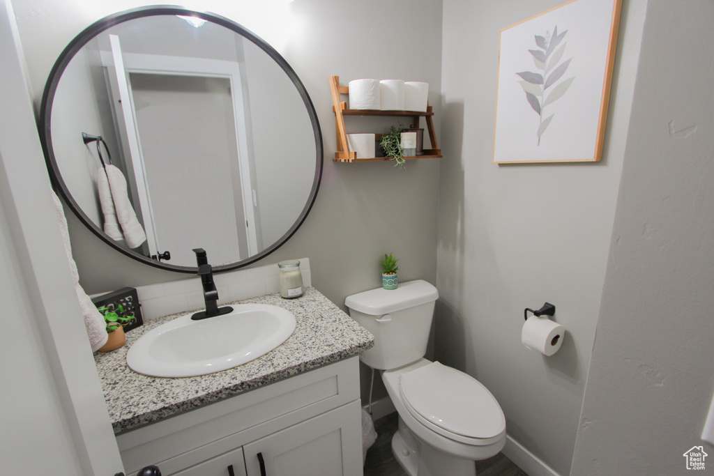 Half bathroom with vanity, toilet, decorative backsplash, and baseboards