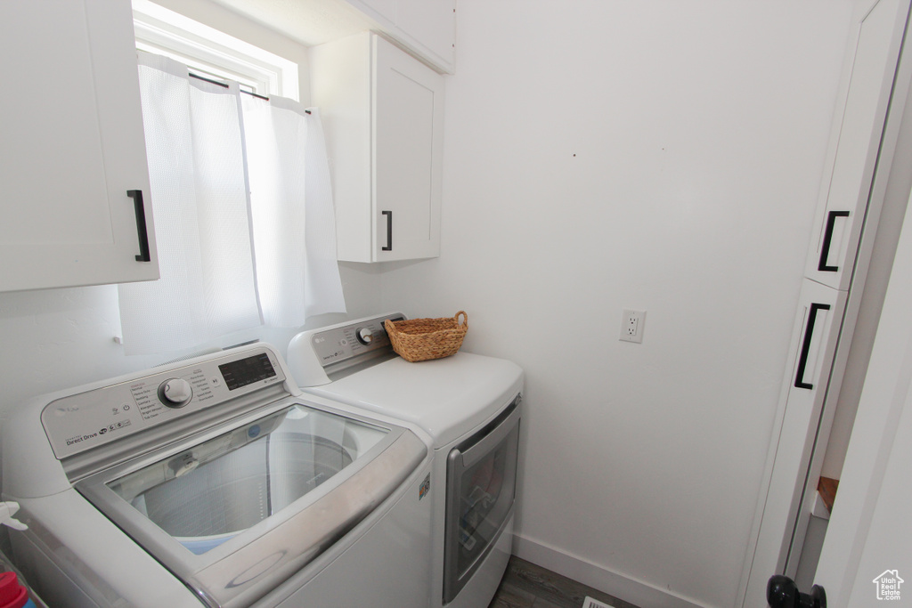 Laundry room featuring cabinet space, washing machine and dryer, baseboards, and wood finished floors