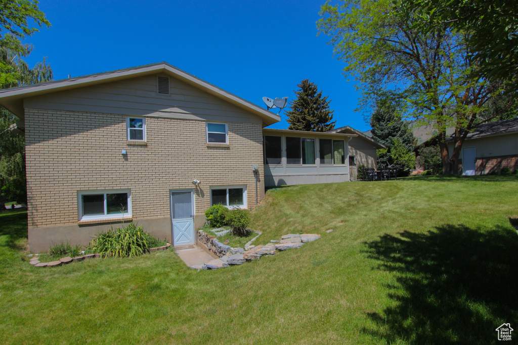 Back of house with a lawn and brick siding