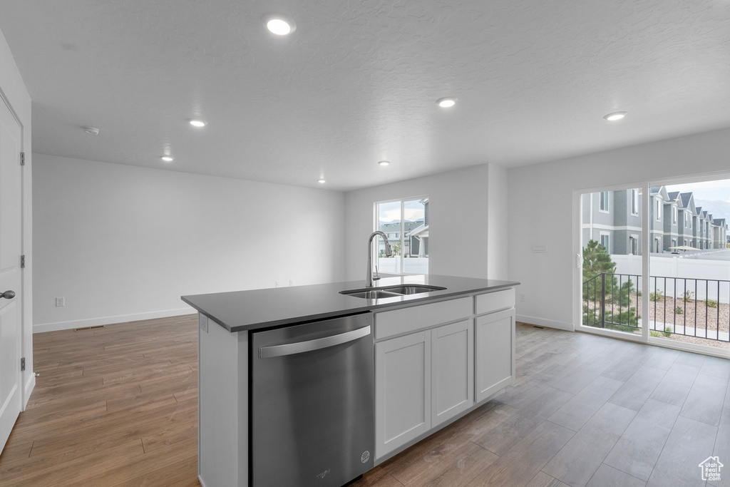 Kitchen featuring dishwasher, a sink, light wood-style floors, recessed lighting, and a center island with sink