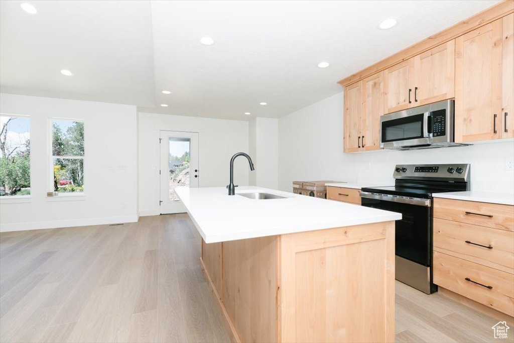 Kitchen with light brown cabinetry, appliances with stainless steel finishes, a sink, light wood-style floors, and an island with sink