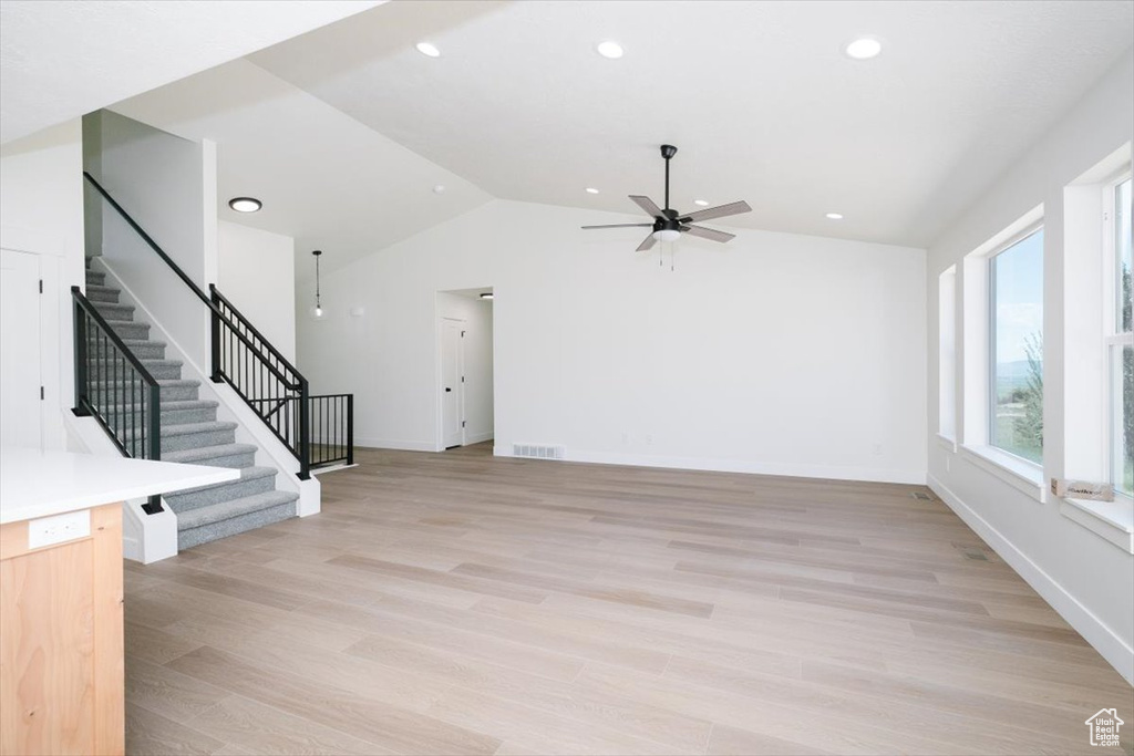 Unfurnished living room with vaulted ceiling, ceiling fan, stairway, light wood finished floors, and recessed lighting