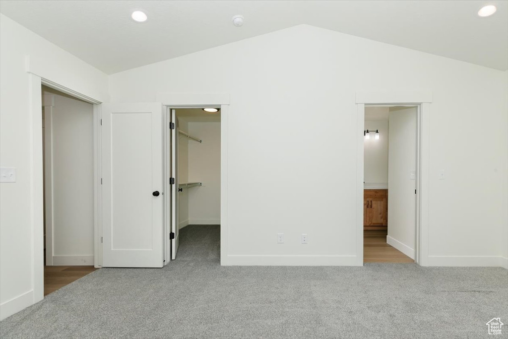 Unfurnished bedroom with carpet, lofted ceiling, a walk in closet, and baseboards