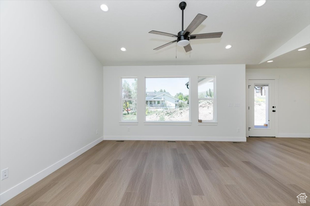 Unfurnished living room with healthy amount of natural light, vaulted ceiling, light wood-type flooring, recessed lighting, and baseboards